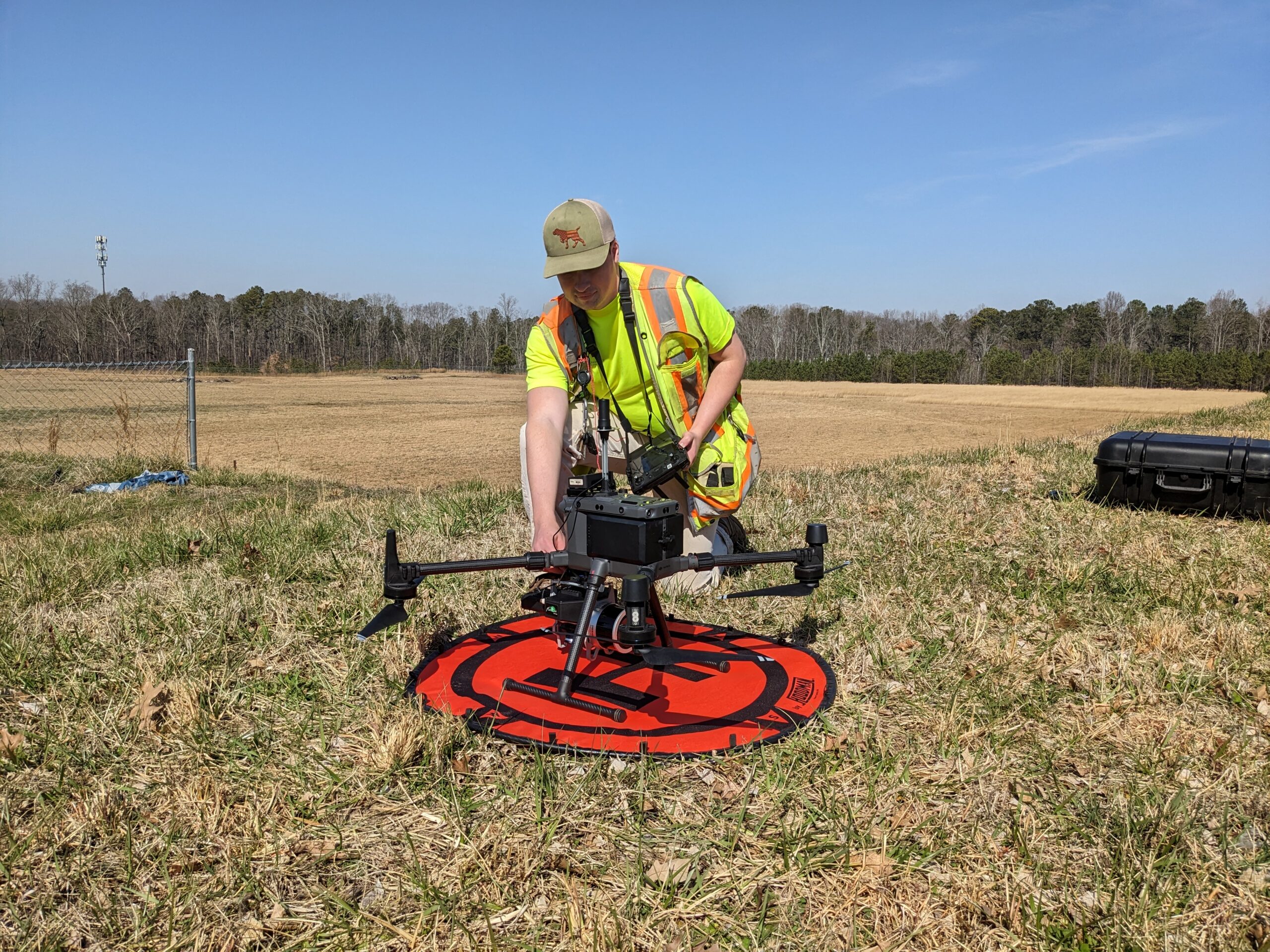 Drone pilot crouching over a surveying drone in an open field.