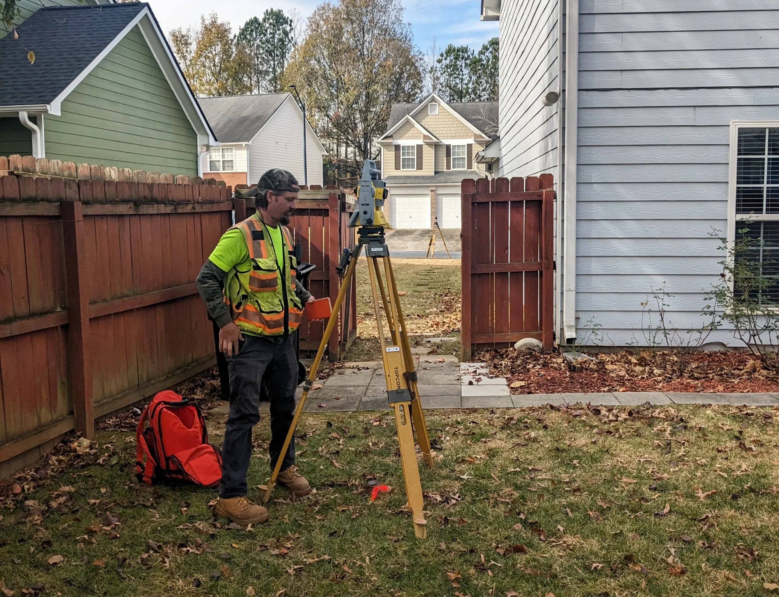 Surveyor reading a survey mapping camera, standing in the back yard of a fenced-in residential home.