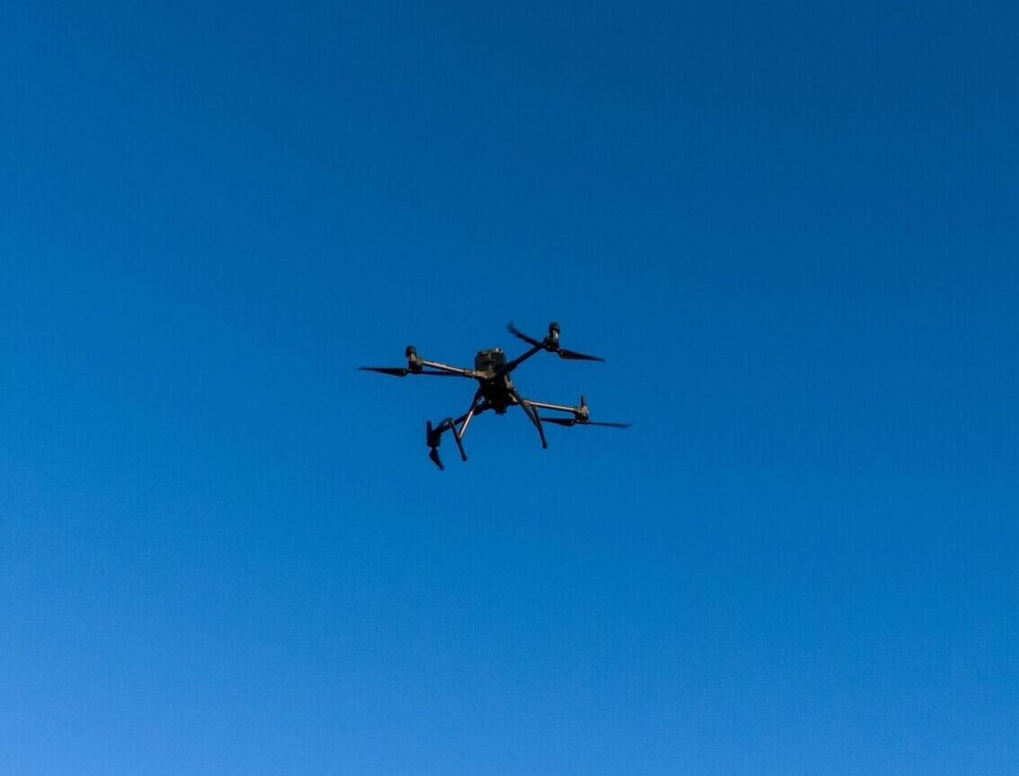 Closeup of a surveying drone flying in a clear, blue sky.
