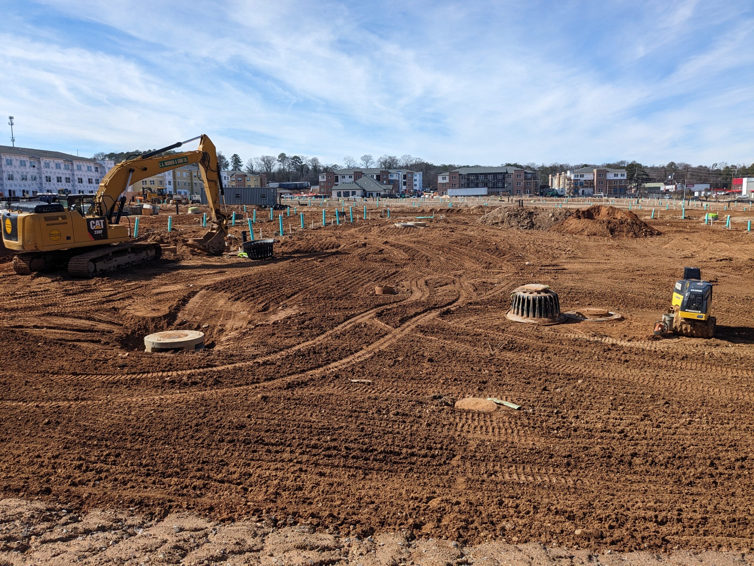A flattened, dirt, residential construction site with a CAT excavator parked on the side.