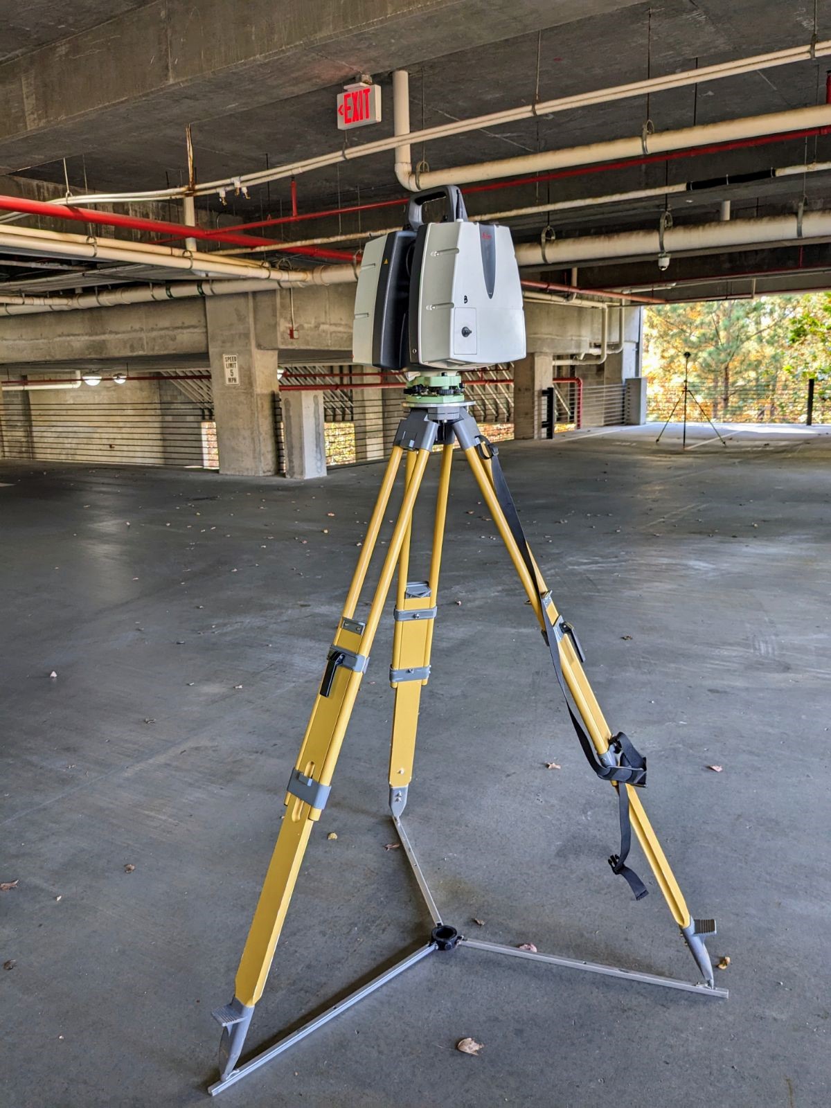A closeup of a survey mapping camera on a tripod sitting inside an empty concrete building.