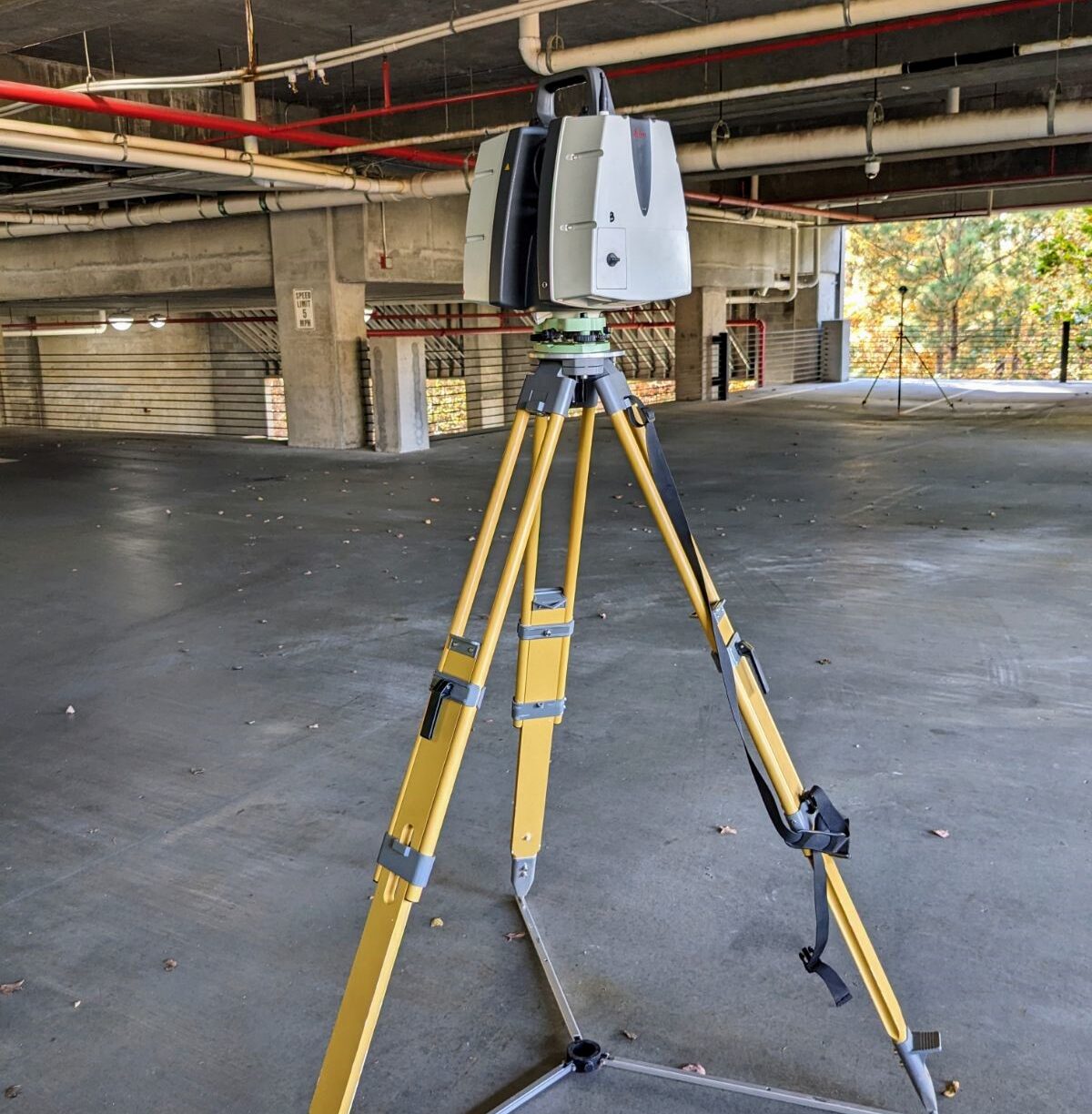 A closeup of a survey mapping camera on a tripod sitting inside an empty concrete building.